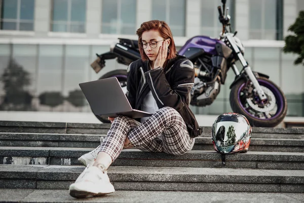 Jovem concentrada senta-se perto de sua moto roxa com seu novo computador — Fotografia de Stock