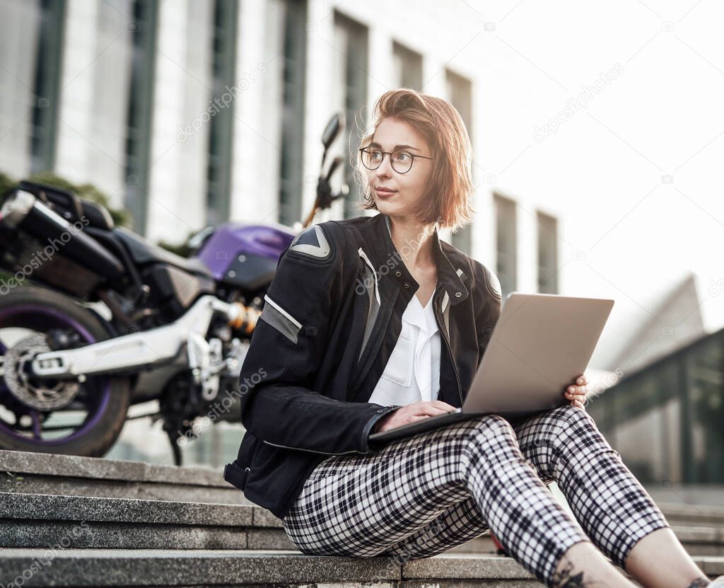 Young girl is sitting next to her purple motorcycle, working at the computer.