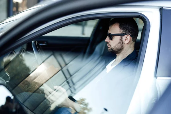 Um empresário adulto está sentado em seu carro novo e navegando algumas notícias — Fotografia de Stock