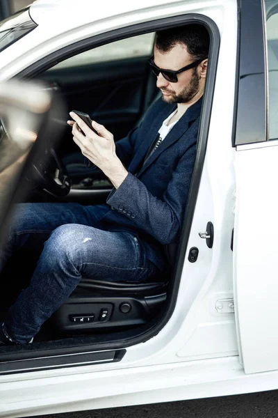 Fashion rich man looking at phone and sitting in the car — Stock Photo, Image