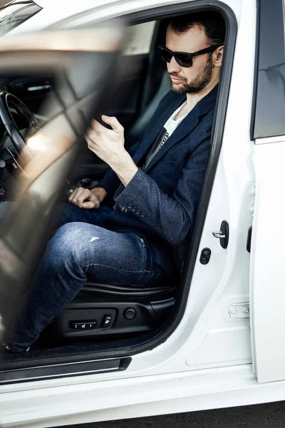 Um empresário adulto está sentado em seu carro novo e navegando algumas notícias — Fotografia de Stock