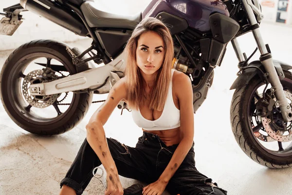 An attractive girl in dirt sirring near sport moto bike — Stock Photo, Image