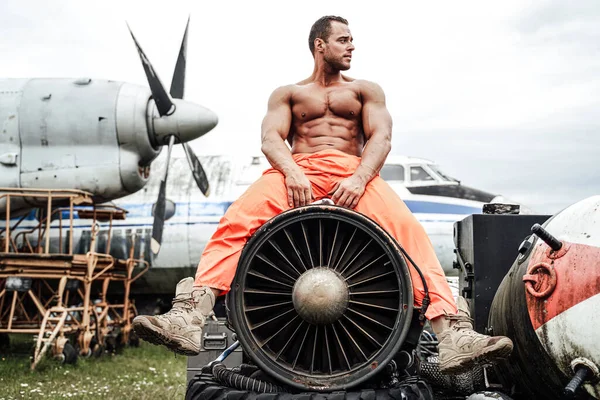 Culturista con grandi bicipiti seduto sulla turbina aeroplani — Foto Stock