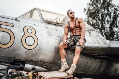 ABD 'li vücut geliştirici arkasında eski bir uçakla uzaklara bakıyor.