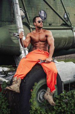 Bronz tenli güçlü adam, fazla gelişmiş helikopterlerin tekerleğinde oturuyor.