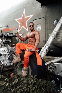 Bronz tenli güçlü adam, fazla gelişmiş helikopterlerin tekerleğinde oturuyor.