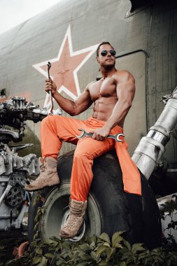 Bronz tenli güçlü adam, fazla gelişmiş helikopterlerin tekerleğinde oturuyor.