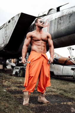 Havaalanında askeri uçakla kalan çekici bir vücut geliştirici.