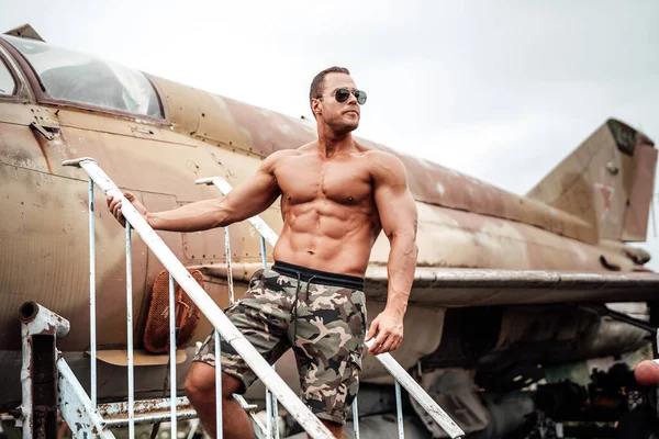Bodybuilder dari Amerika Serikat melihat jauh dengan pesawat tua di belakang — Stok Foto