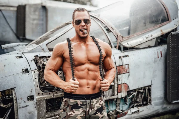 Strong tanned guy smoking cigar with airplane behind — Stock Photo, Image