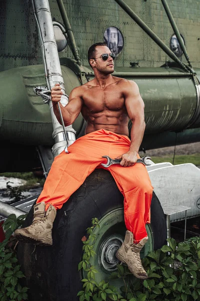 Bronz tenli güçlü adam, fazla gelişmiş helikopterlerin tekerleğinde oturuyor.