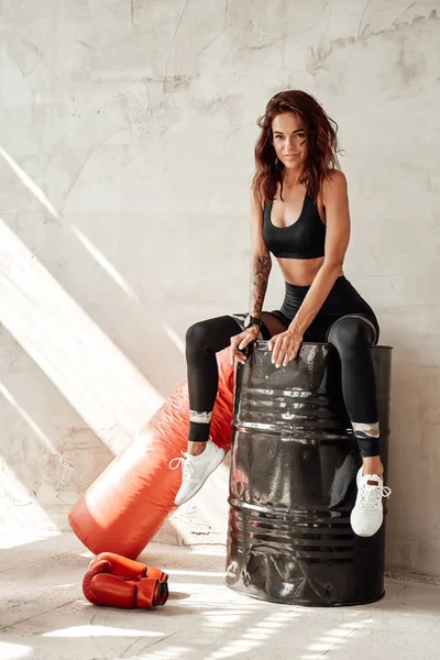 Mulher magro em sportswear preto sentado no barril — Fotografia de Stock