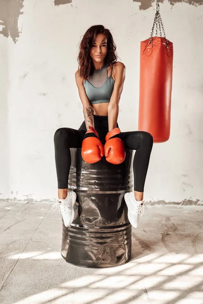 Eldivenli sıska kadın arkada çantasıyla namluda oturuyor.