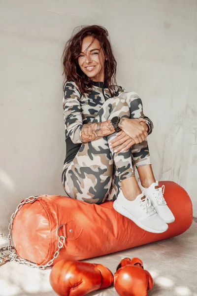Mujer en ropa de deporte de camuflaje sonriendo y sentada en la bolsa — Foto de Stock