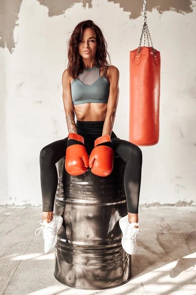 Bronzlaşmış kız varilde oturuyor ve beyaz duvarlar arkasında