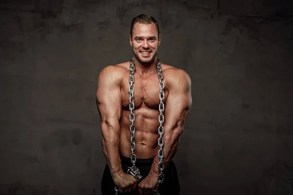 Hombre con enormes bíceps y cadenas posando en estudio —  Fotos de Stock