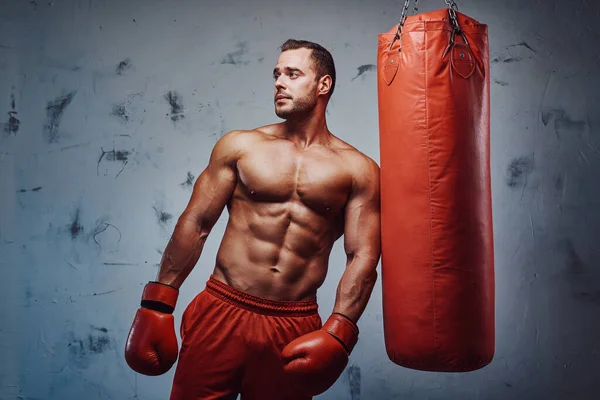 Muskulös man med naken överkropp poserar med boxningssäck — Stockfoto