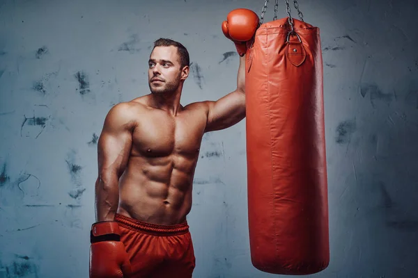 Hombre fuerte y seguro que se queda cerca de la bolsa con guantes de boxeo — Foto de Stock