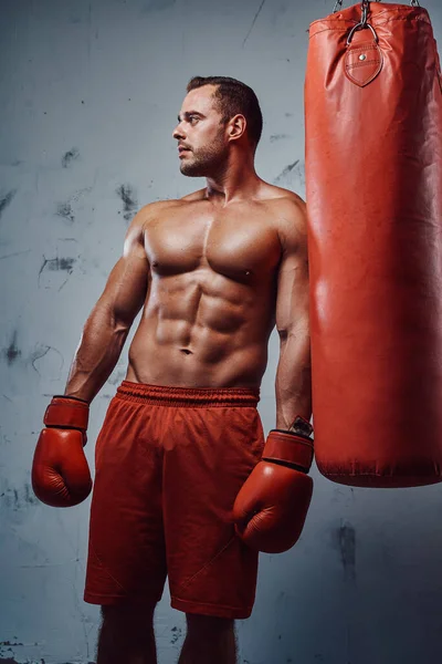 Мускулистый мужчина с обнаженным туловищем, позирующий с боксерской грушей — стоковое фото