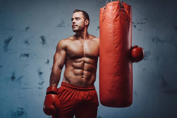Boxeador masculino brutal que se queda con guantes y saco de boxeo —  Fotos de Stock