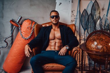 Güneş gözlüklü zalim adam, özel odada sandalyede oturuyor.