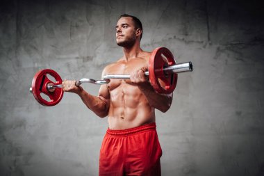 Kaslı elli sporcu arka planda halteri kaldırıyor.