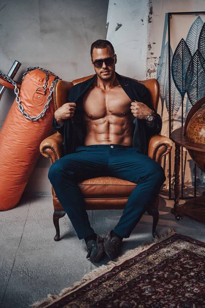 Koltuğunda çıplak poz veren kaslı adam.