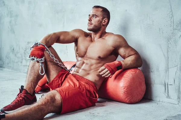 Muscular boxer resting after workout on floor with bag — Stock Photo, Image