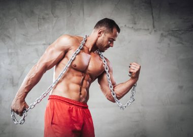 Zincirlerle poz veren şekilli vücutlu zalim bir adam.