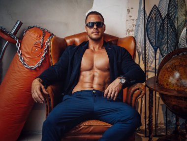 Güneş gözlüklü zalim adam, özel odada sandalyede oturuyor.