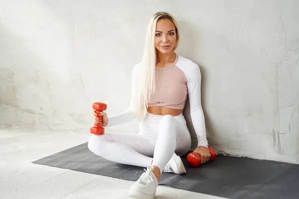 Mujer en ropa deportiva blanca posando en la alfombra en la habitación con plantas —  Fotos de Stock