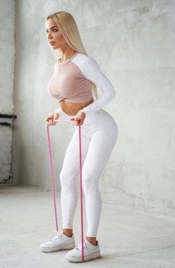 Güzel bir kadın ışık odasında lastikle egzersiz yapıyor.