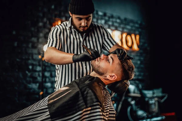 Peluquero profesional cortando barba de su cliente en salón —  Fotos de Stock
