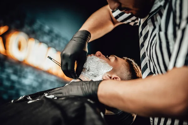 Caucasien coiffeur rasage un client dans le salon élégant — Photo