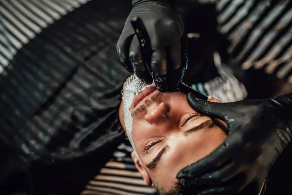 Vakkundige kapper scheren een klanten baard in saloon — Stockfoto