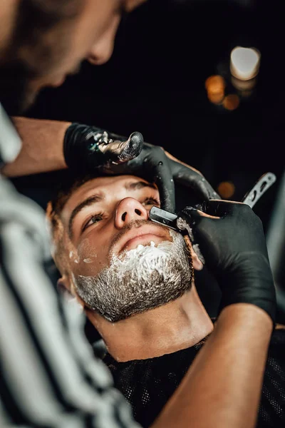 El barbero hábil afeitando la barba de los clientes en el salón —  Fotos de Stock
