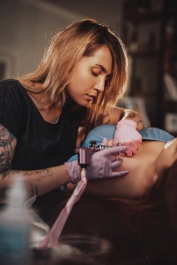 Kadın dövme ustası dairesinde müşterisini resmediyor.