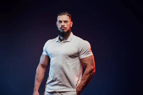 Bearded bodybuilder in shirt posing in dark background