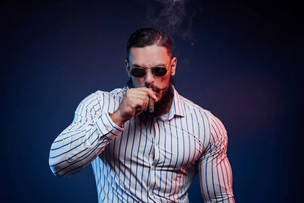 Brodaty gangster palenie cygaro i pozowanie w ciemnym tle — Zdjęcie stockowe