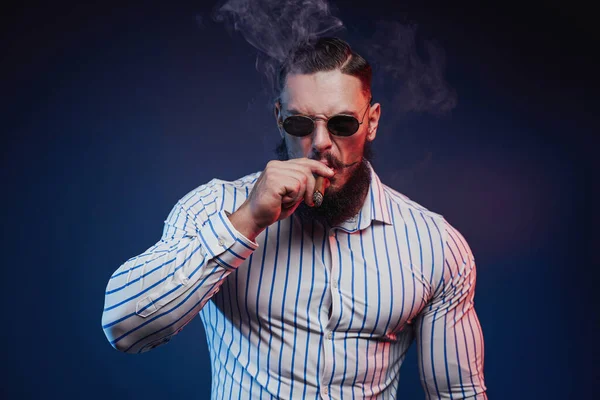 Barbudo muscular cara em vidro fumando charuto e posando — Fotografia de Stock
