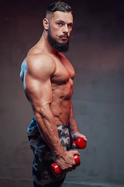 Tipo musculoso con barba sosteniendo pesas y posando en el estudio — Foto de Stock