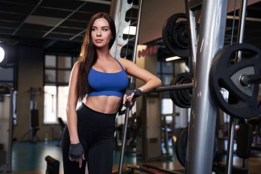 Spor salonunda çekici esmer, eğik halterle poz veriyor.