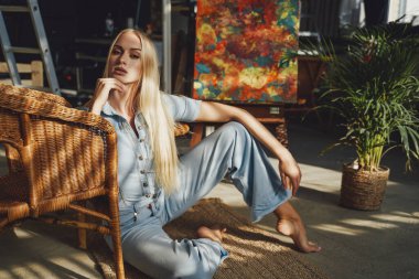 Güzel sarışın oteldeki sandalyeye yaslanmış halının üzerinde dinleniyor.