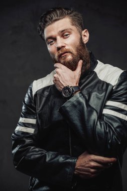 Koyu renk arka planda poz veren deri ceketli saçlı adam.