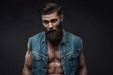 Cool bearded man in jeans jacket posing in studio clipart