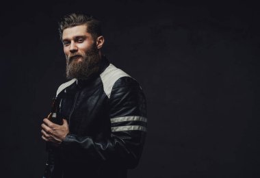Sakallı adam, arka planda siyah bir şişeyle poz veriyor.