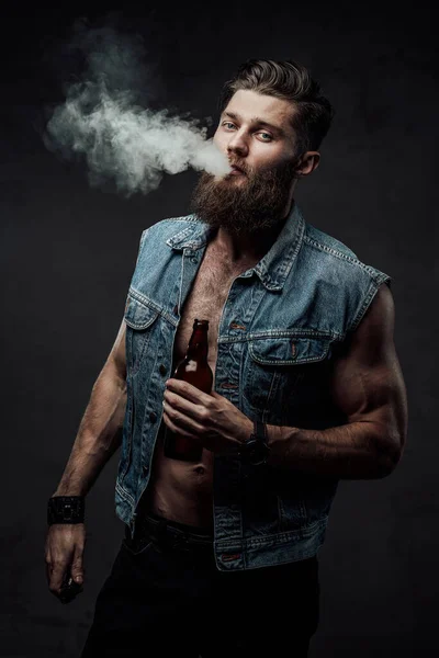 Brutální muž kouření vape v bundě s vousy v tmavém pozadí — Stock fotografie