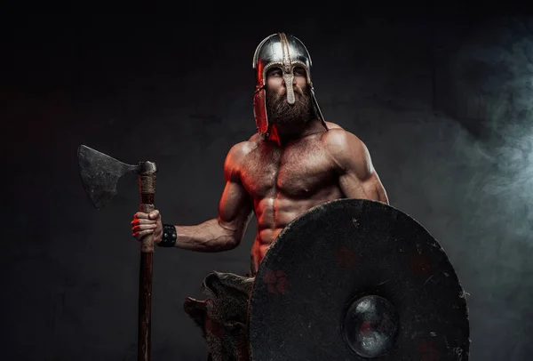 Warlike viking poseren met bijl en schild in donkere achtergrond — Stockfoto