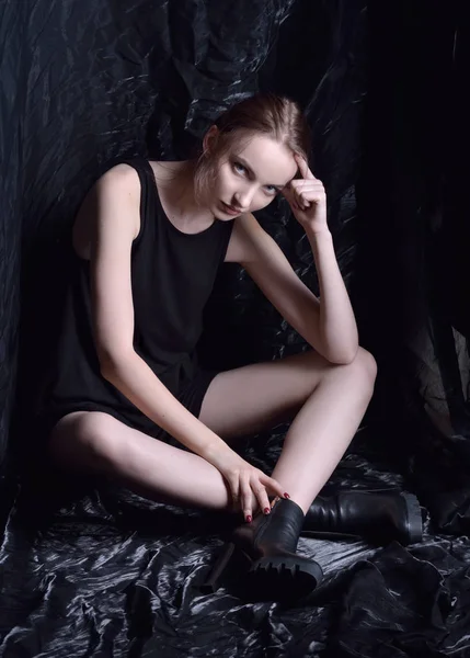 Sitting beautiful woman in black top and shoes  in dark studio. — Stock Photo, Image