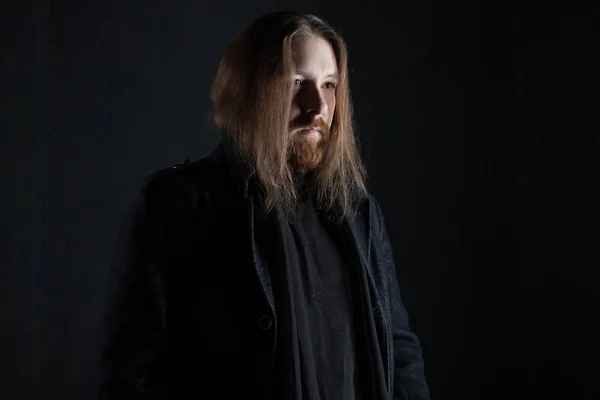 Portrait d'homme aux cheveux longs et à la barbe en vêtements noirs sur fond sombre — Photo